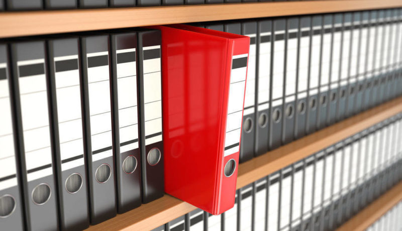 Red file office binder on a shelf full of black office binders